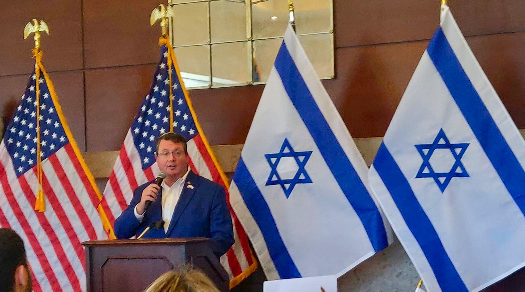 A politician stands in front of U.S. and Israeli flags